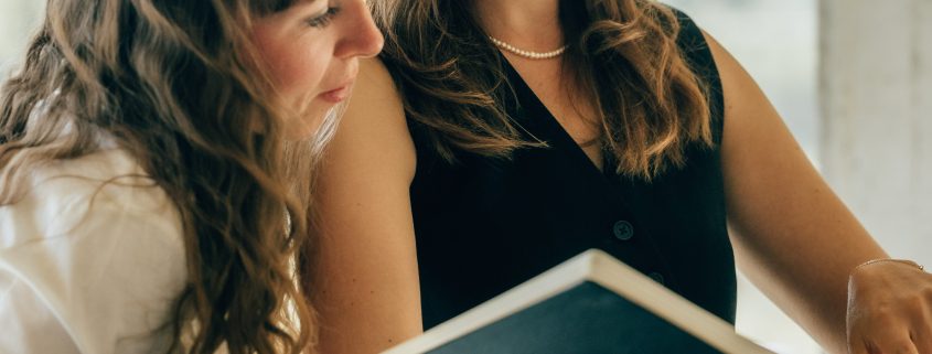 Anna Ebmeyer zeigt einer Kundin Schriften aus einem Skizzenbuch, während sie beide im Stehen im Gespräch sind